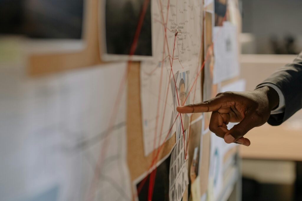 Close-up of an investigator pointing at an evidence board with connected clues using red strings.