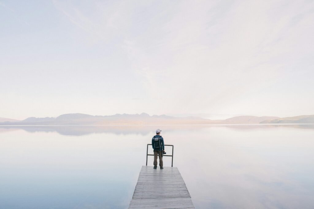 A solitary traveler stands on a dock enjoying the serene water view