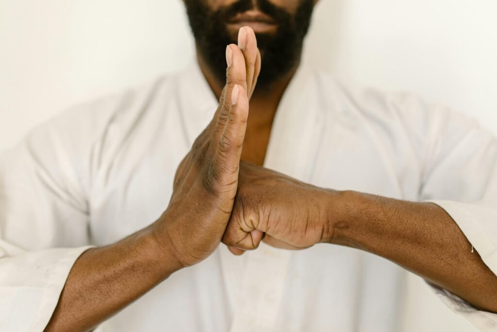 Close-up of a martial artist in traditional white gi performing a greeting pose indoors.