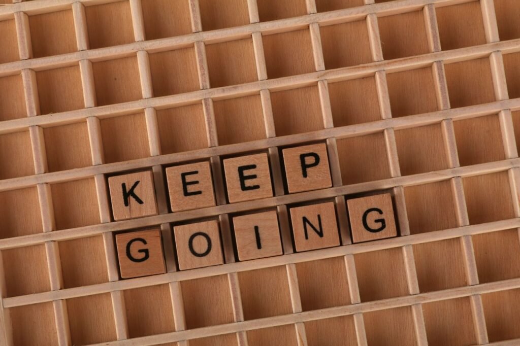 Keep going message spelled with wooden blocks on a wooden grid background.